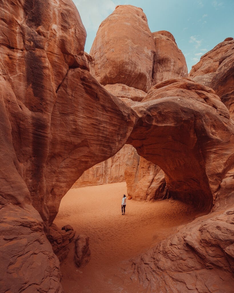 female hiker walking under sand dune arch arches national park utah