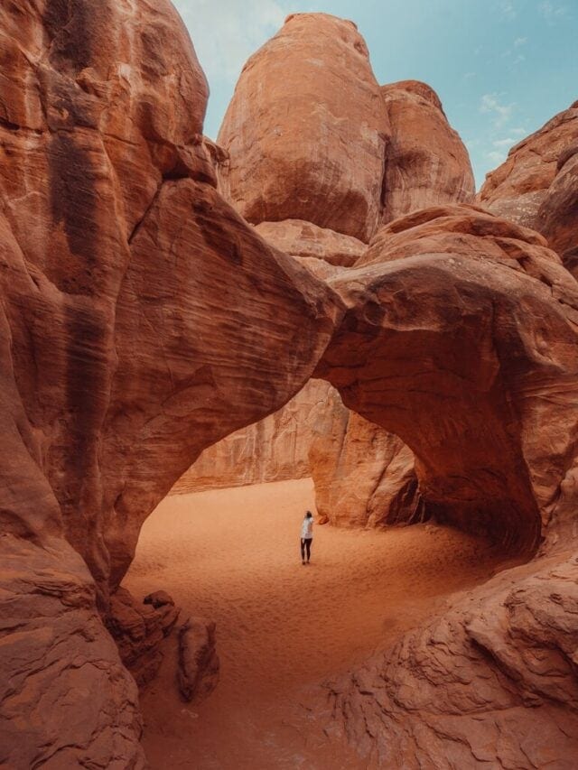 female hiker walking under sand dune arch arches national park utah