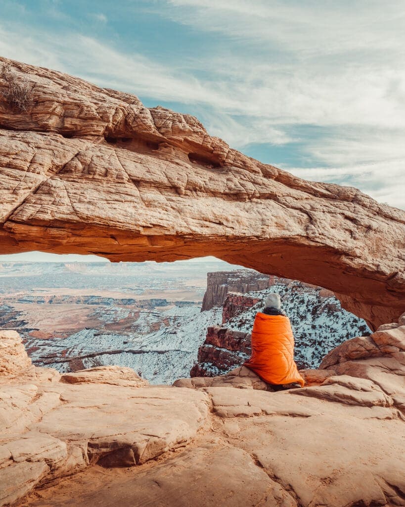 girl sitting under mesa arch in canyonlands national park in the winter