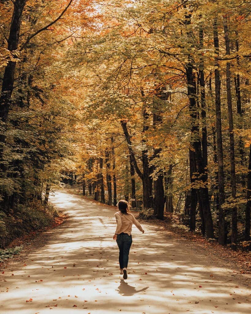 girl running through golden yellow fall foliage in stowe vermont 